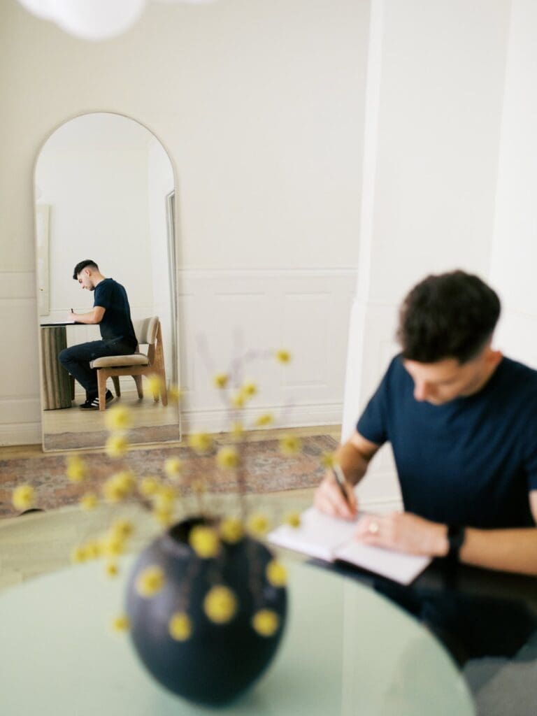 A counselor writes in a journal beside a mirror and yellow flowers.