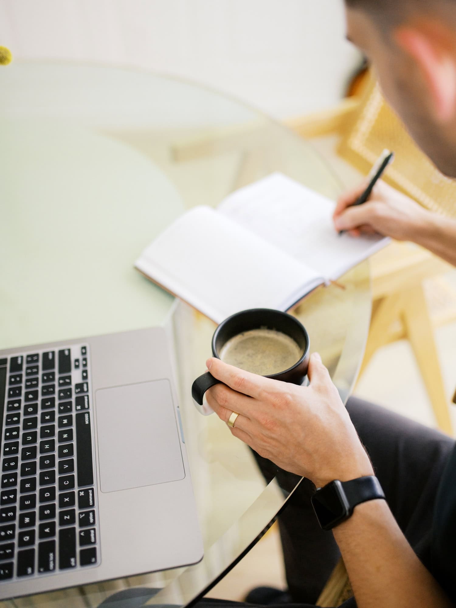 A counselor writes in a notebook beside a laptop and coffee mug.
